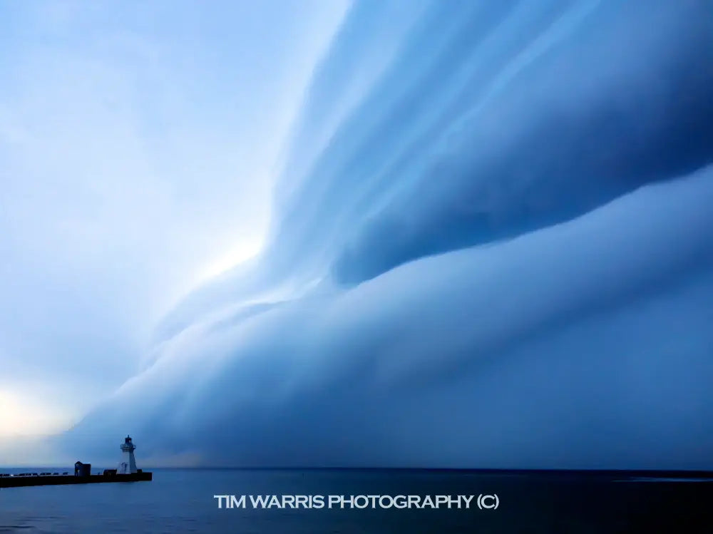 Silhouette of lighthouse at twilight with dramatic blue sky and faint rainbow arc over dark water